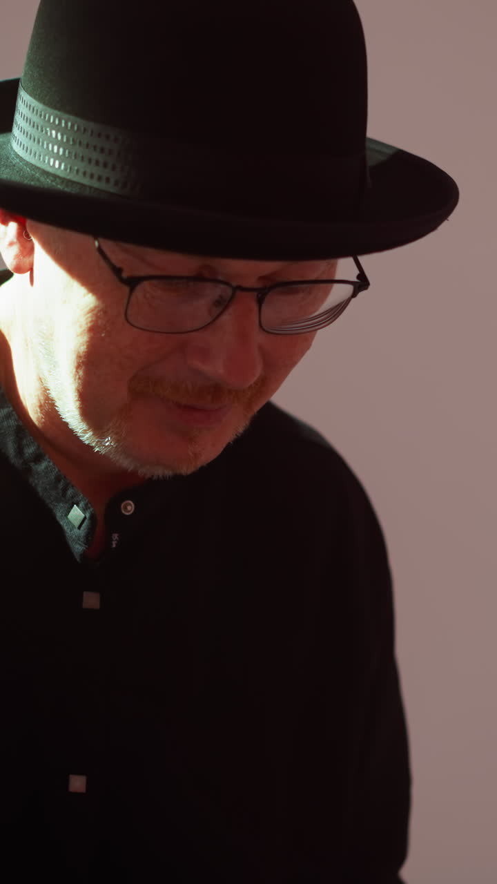 부드러운 분홍색 배경에 검은 옷과 모자를 입은 남자의 클로즈업, 사려 깊게 내려다보고