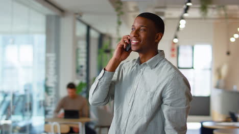 businessman standing in modern open plan office talking on mobile phone