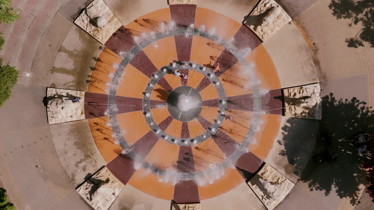 Top-down view of a water fountain in Chattanooga, Tennessee, with concentric rings, spraying streams, and families enjoying summer fun