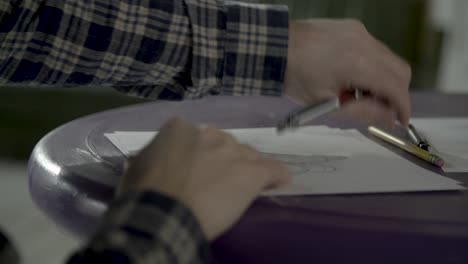 sketch artist moving around sketch paper on a table before continuing to draw.
