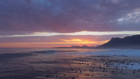 drone flies over ocean and rolling waves into the setting sun with seagulls flying overhead