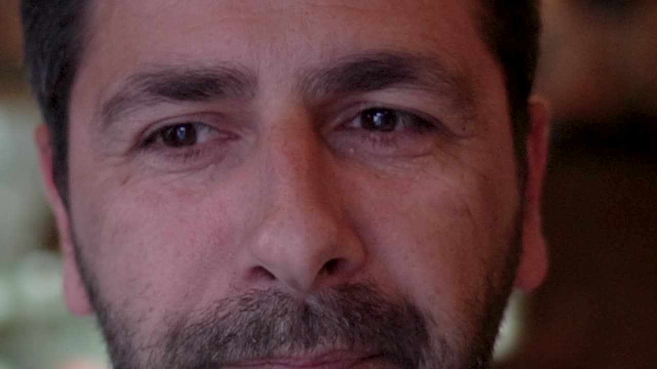 un hombre sonriente y de buena disposición con una capucha en la cabeza, mira a la habitación y come una comida tradicional