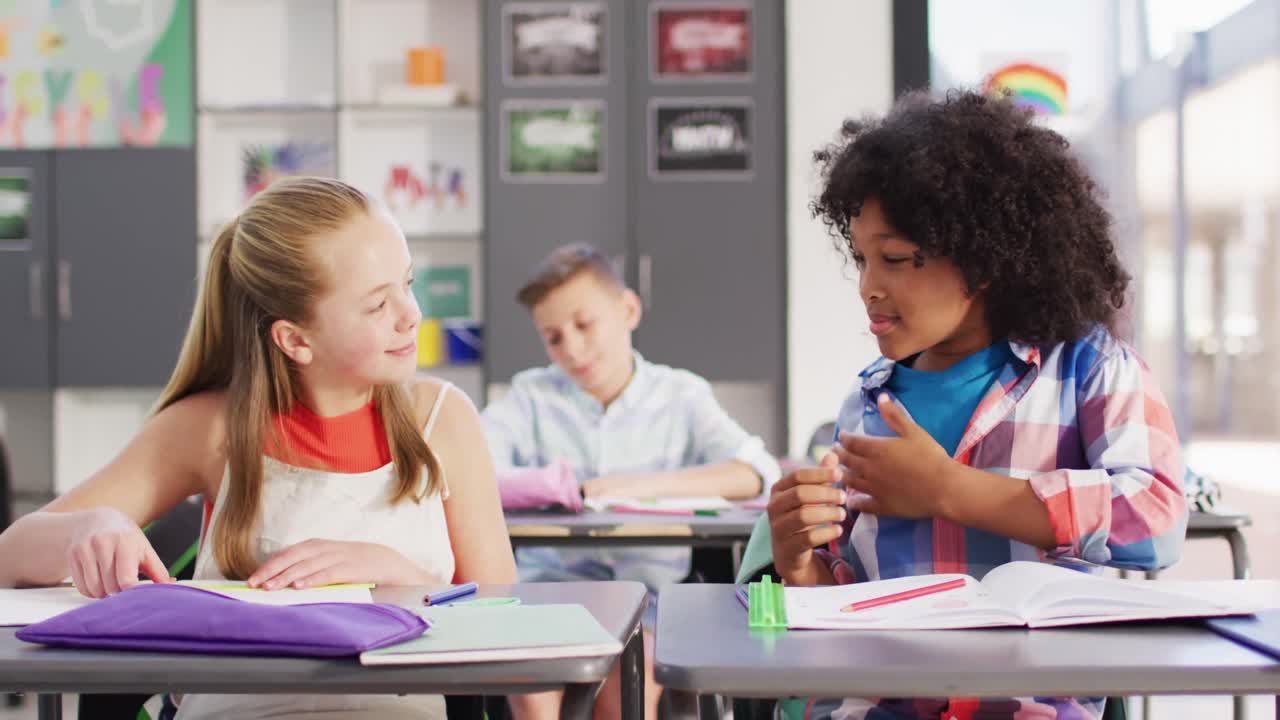 Diverse happy schoolchildren at desks learning sign language in school classroom