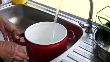 chef turns on faucet and fills up red cooking pot with water for boiling