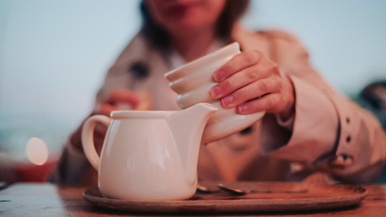 A woman emptying the cup back into the teapot, creating a fluid motion over a wooden tray