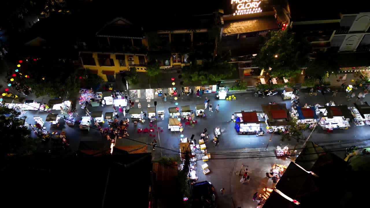 From above, view of night market in Hoi An, Vietnam with rush of people, stalls and glowing lanterns.