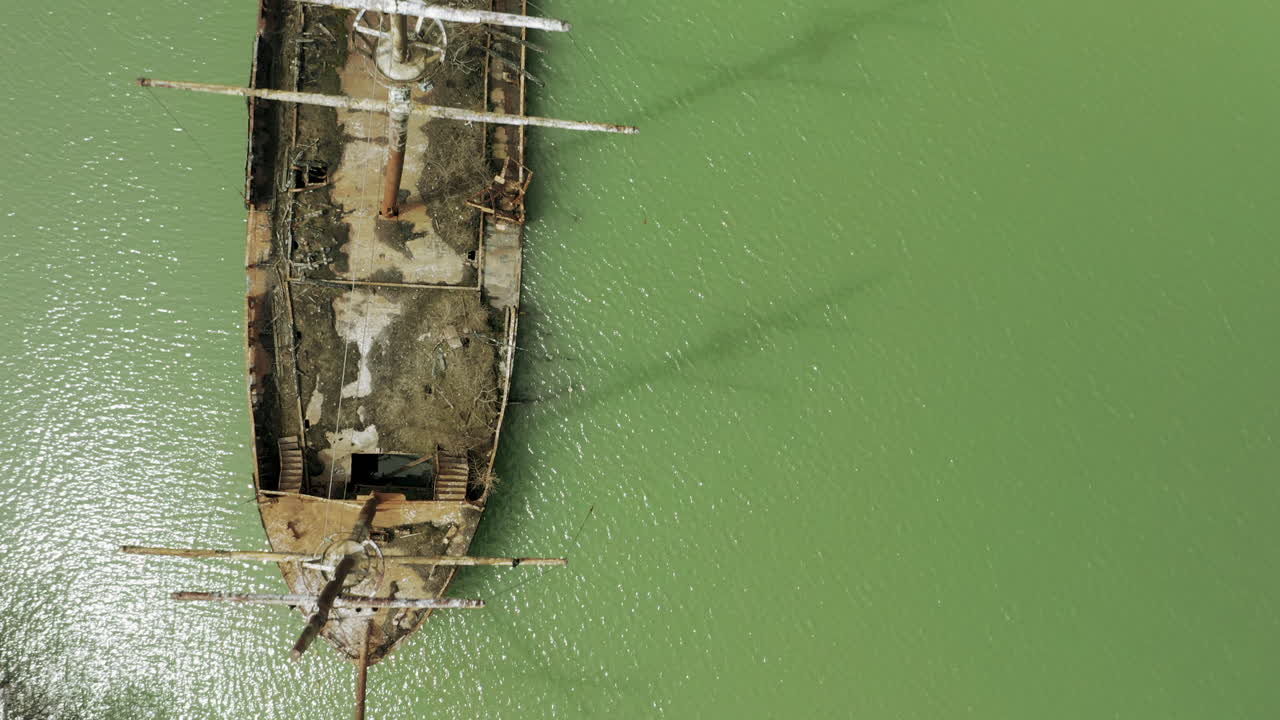 Rusty red shipwreck stuck in shallow green water