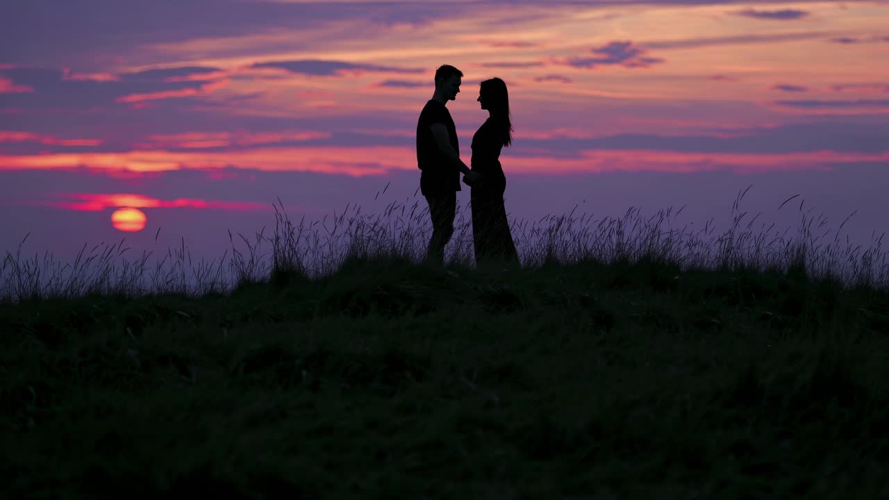 Silhouetted couple holding hands at sunset on a hilltop
