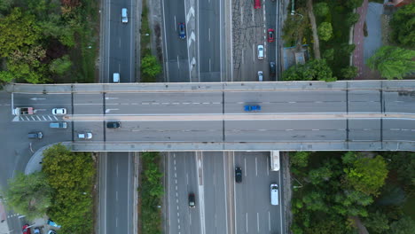 vertical drone shot capturing fluid traffic on a busy highway interchange and overpass. vehicles smoothly passing on multiple lanes, surrounded by lush greenery, emphasizing urban transportation