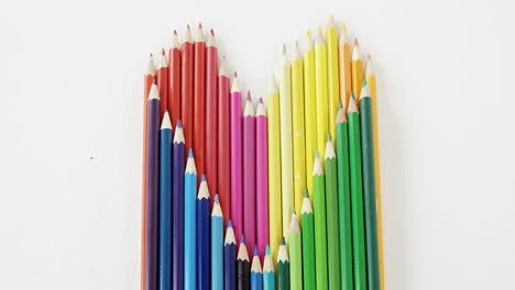 lápices de colores dispuestos en forma de corazón sobre un fondo blanco