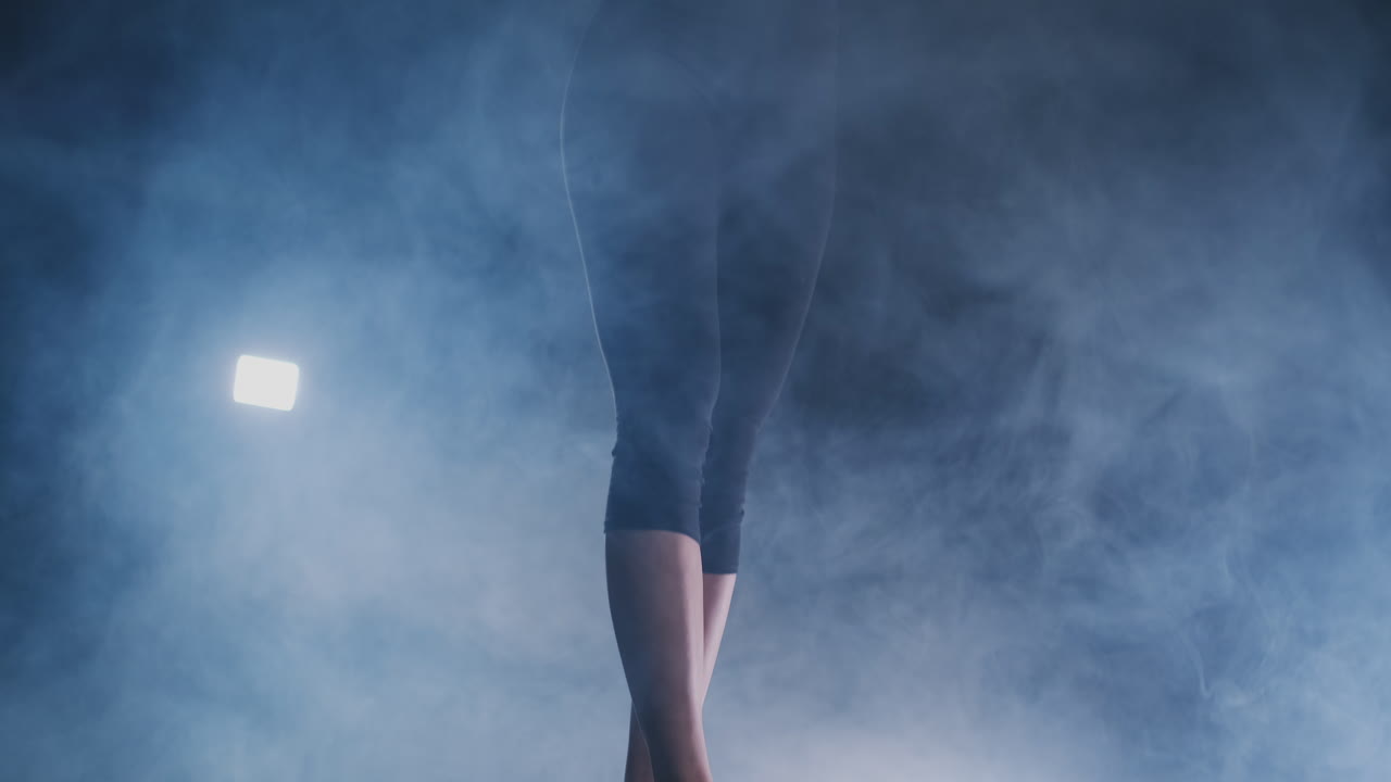 Close-up of the foot of a professional gymnast girl jumping in slow motion in the smoke on a balance beam. Women's gymnastics. Grace and a healthy lifestyle