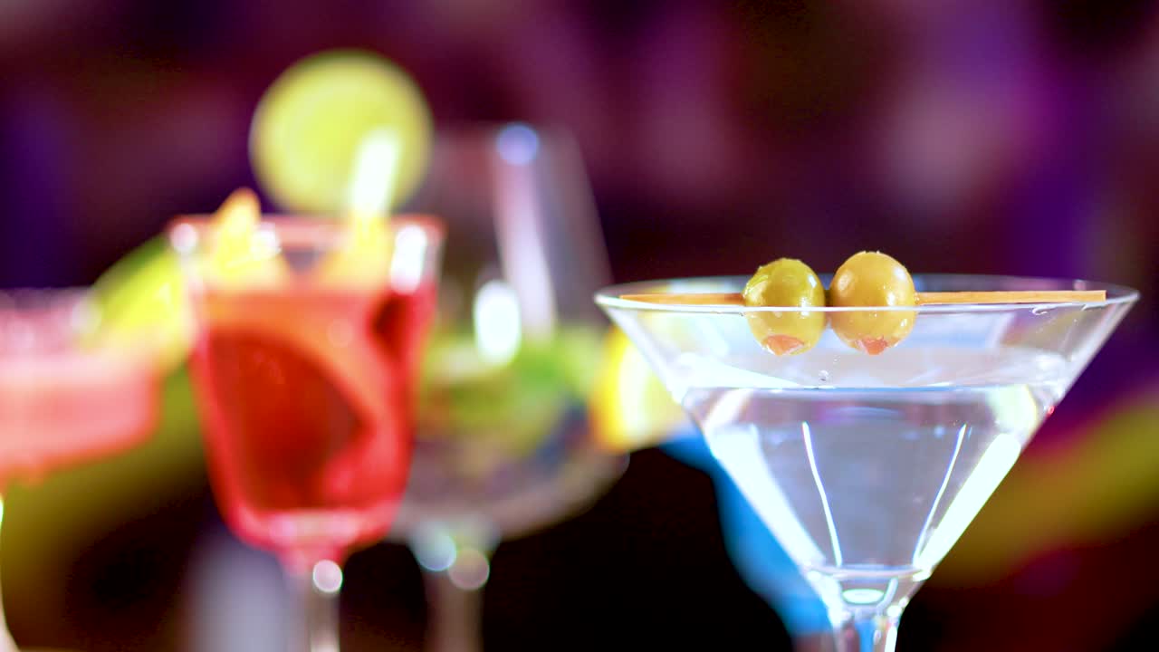 A martini cocktail is garnished with olives in a vibrant bar setting, highlighting colorful drinks and lively atmosphere