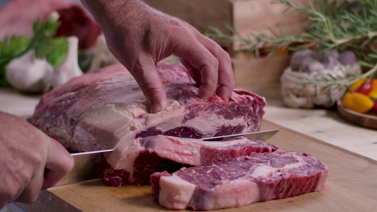 Close up seorang tukang daging yang mengukir steak ribeye berlemak tinggi untuk diet ketogenik dari daging sapi panggang mentah di atas papan kayu