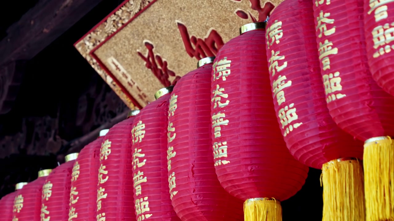En række røde lanterner, prydet med guldbogstaver og gule kvaster, hænger fremtrædende i et tempel i Shanghai. Ideel til kulturelle dokumentarer eller rejseindslag.