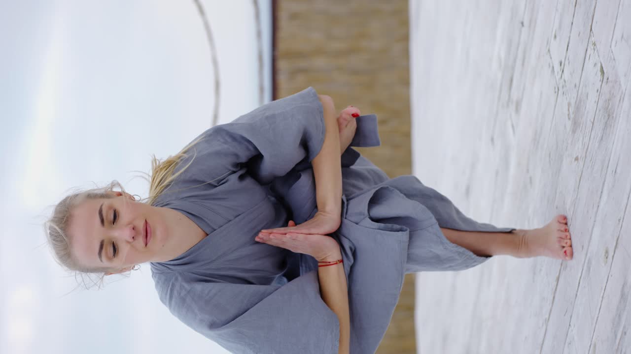 로브를 입은 매력적인 금발 여성이 야외에서 요가 에카 파다 우트카타사나를 하고 있습니다.