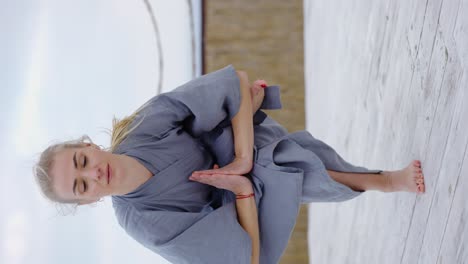 attractive blonde woman in robe doing yoga eka pada utkatasana outdoors