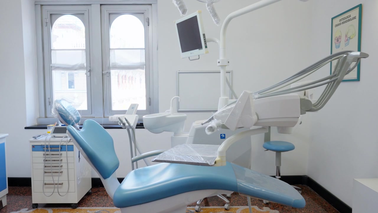 Moderna sala per trattamenti dentali con poltrona blu, attrezzature e luce naturale dalla finestra