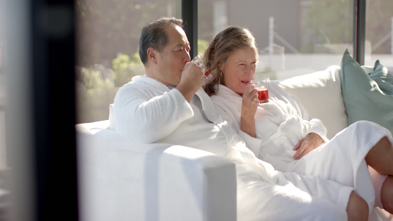 Relaxing on couch, senior couple in bathrobes drinking tea together
