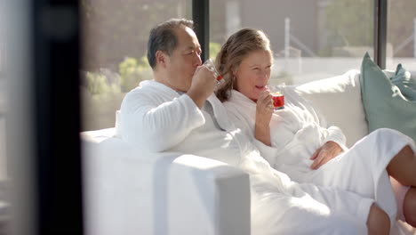 relaxing on couch, senior couple in bathrobes drinking tea together