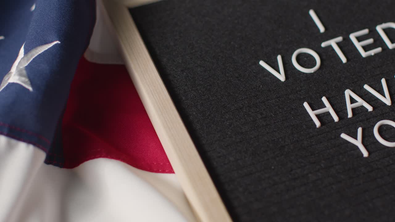 Close Up Of Sign Reading I Voted Have You Lying On US Stars And Stripes Flag For American Election 2024