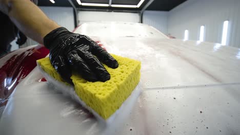 man worker washing red car on a car wash with yellow washcloth.