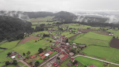 Aerial-Circle-over-a-small-town-surrounded-by-trees-and-mountains-in-Valle-De-Bravo,-Mexico