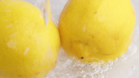 gotas de agua fluyen hacia limones amarillos en cámara lenta