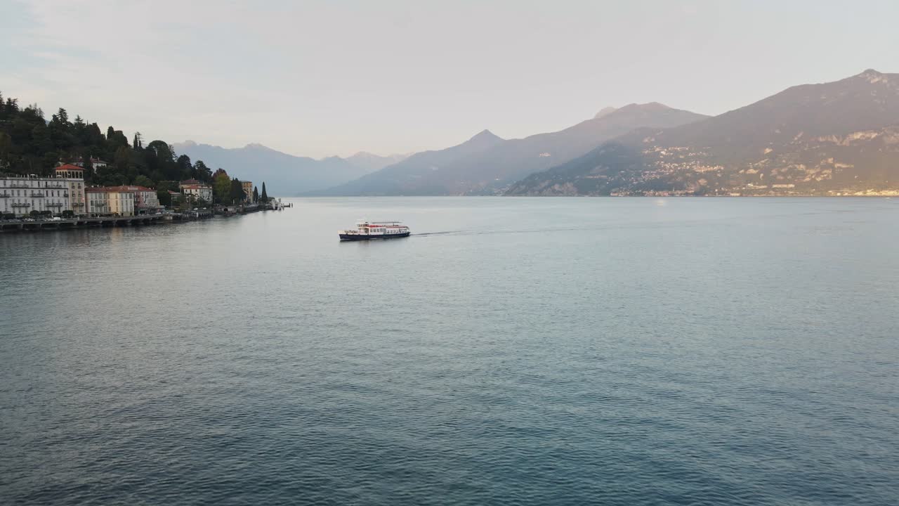 A beautiful drone shot at Lake Como, moving forward as a boat passes by. The tranquil lake and majestic mountains in the background complete the picturesque scene.