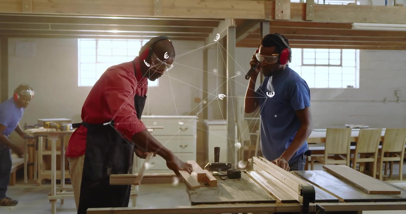 Instructor tapping trainee shoulder guiding plank through saw for safe woodworking, dust swirling