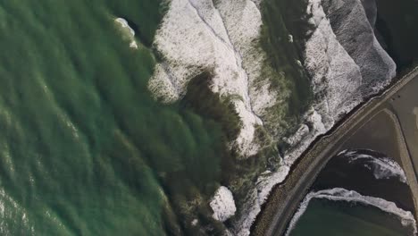 aerial view green ocean waves breaking top down with white foam onto brown beach