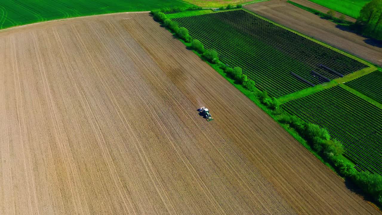 vista aérea de un tractor cultivando extensas tierras de cultivo con vegetación verde vibrante y paneles solares