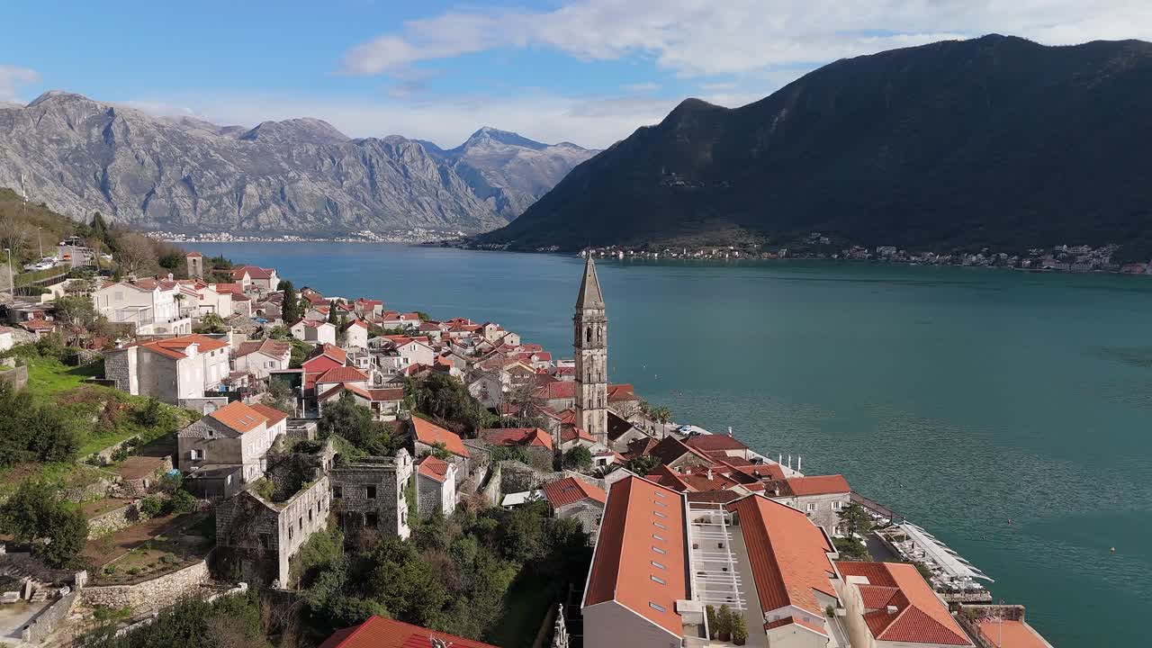 4K drone footage captures Saint Nicholas Church in the charming town of Perast, Montenegro, with a beautiful view of the UNESCO-listed turquoise Bay of Kotor and mountains in the background