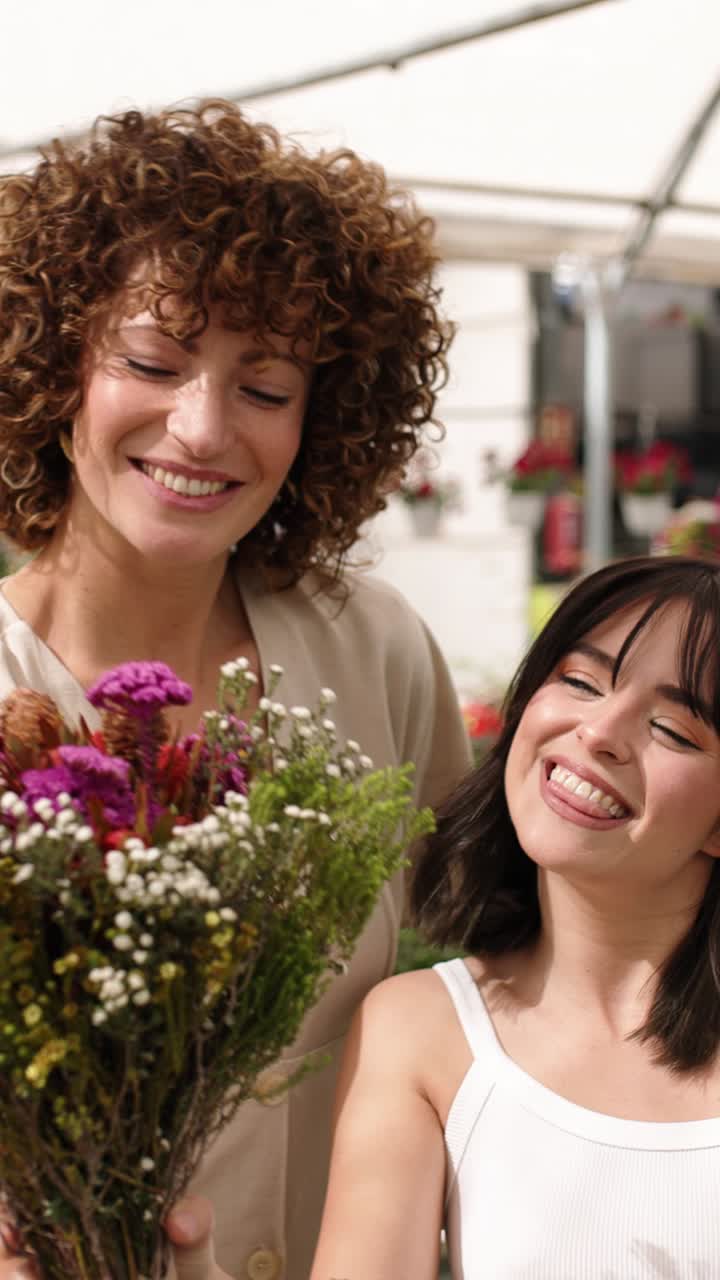 Two happy women smelling and showing a bouquet of flowers. Vertical