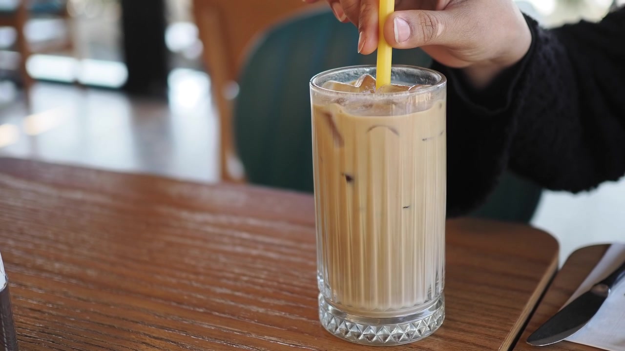 Mano che mescola caffè freddo con una cannuccia gialla su un tavolo di legno