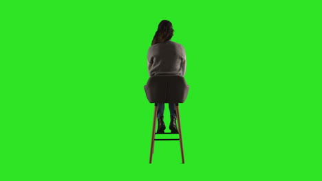 Vista-Trasera,-Fotografía-De-Estudio-De-Una-Mujer-Sentada-En-Un-Taburete-De-Espaldas-A-La-Cámara-Contra-Una-Pantalla-Verde