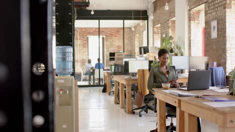 happy african american casual businesswoman using smartphone and having lunch in office, slow motion