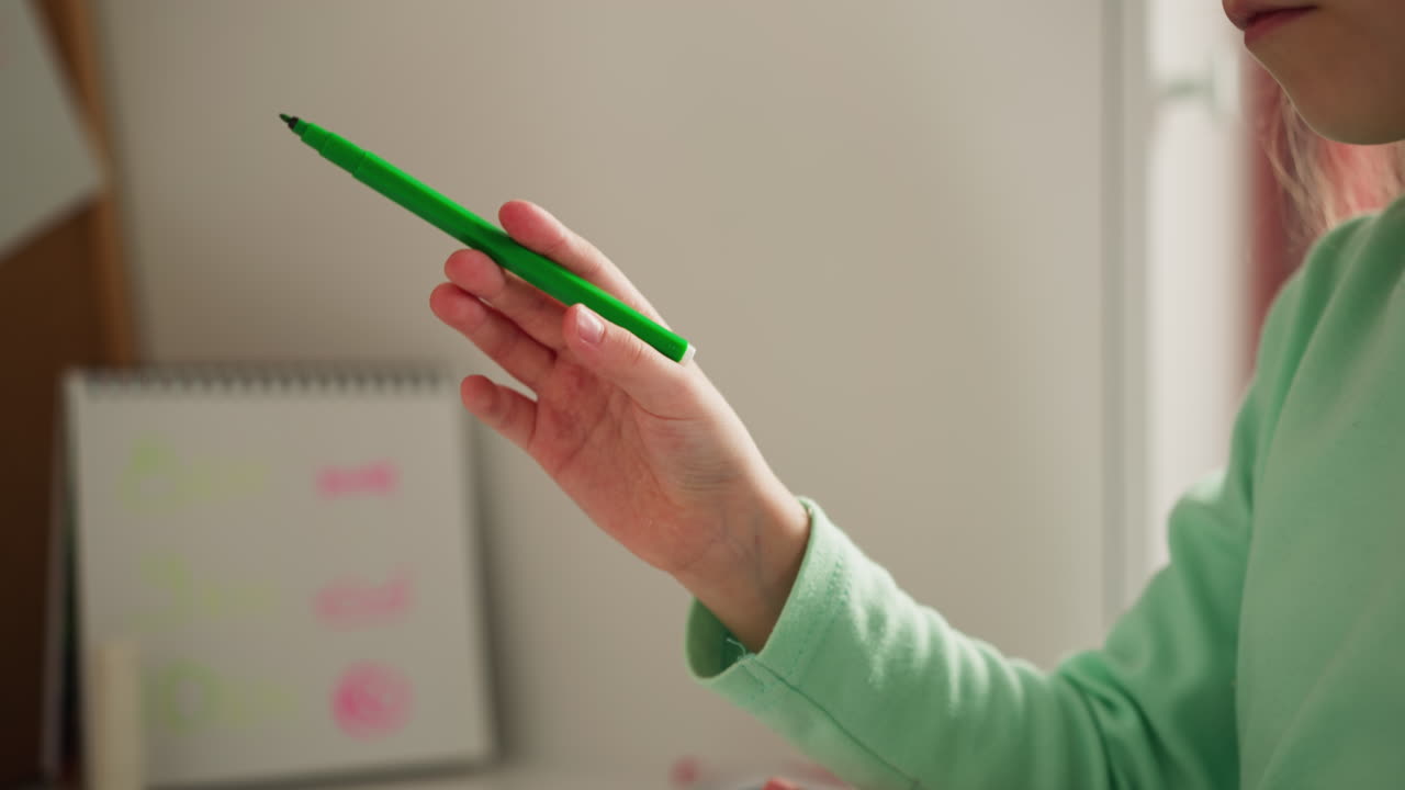 Girl removes cap from green felt-tip pen drawing picture