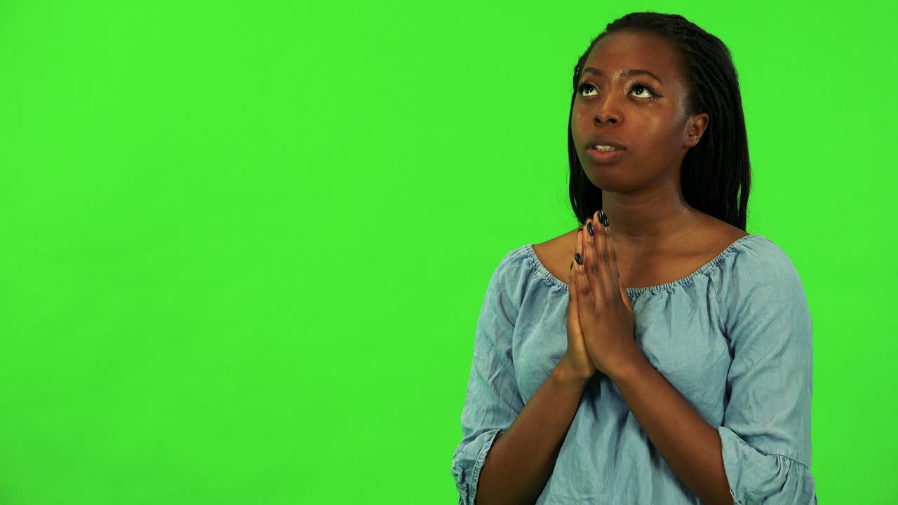 A young black woman prays with hands clasped together - green screen studio