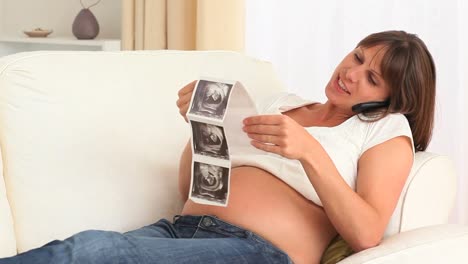 pregnant woman holding a scan of her baby and telephoning