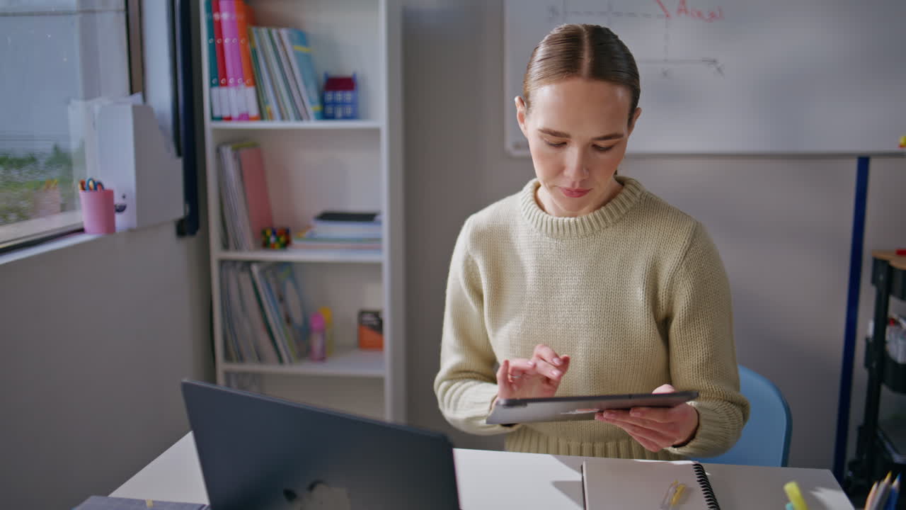 Focused teacher using tablet at school workplace closeup. Serious woman working