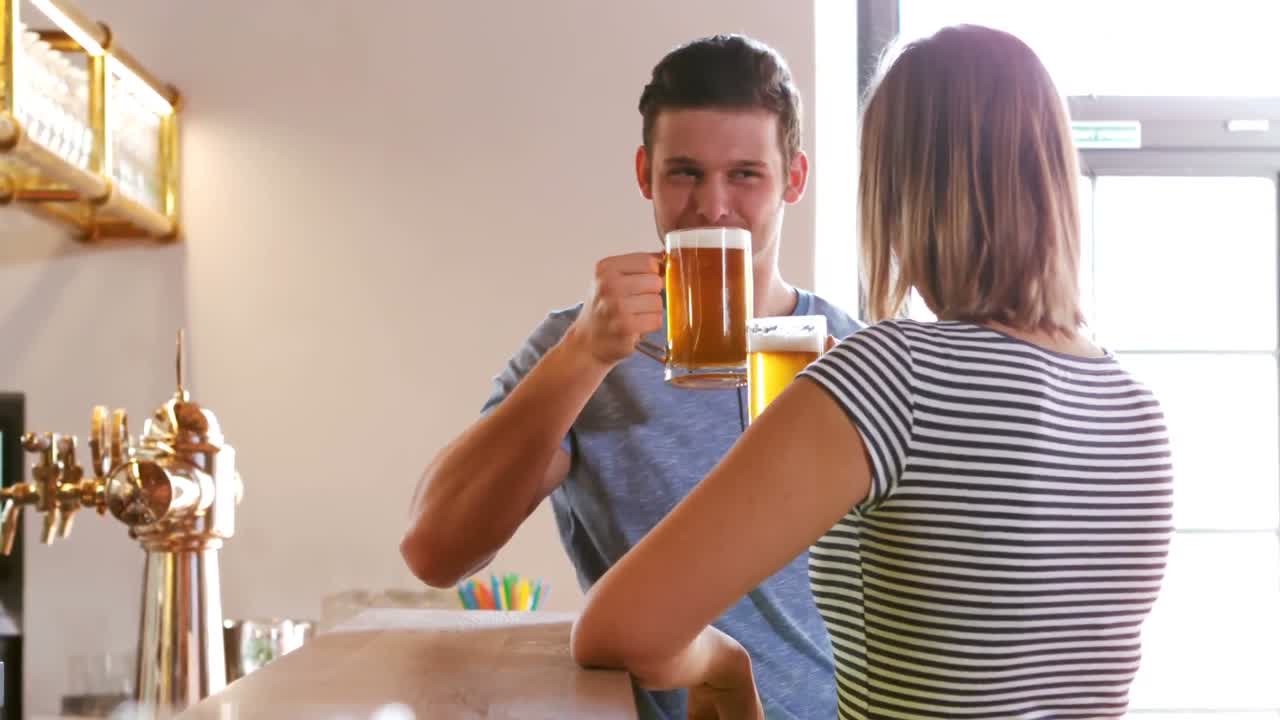 Couple interacting while toasting a glass of beer at bar counter