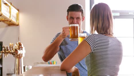 Couple-interacting-while-toasting-a-glass-of-beer-at-bar-counter