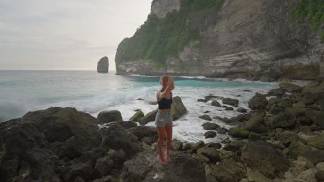 cheering female tourist taking selfie on rocky shore in nusa penida secluded beach