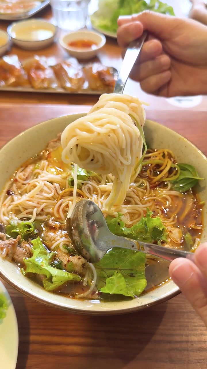 Primo piano di mani che usano un cucchiaio e una forchetta per sollevare i noodles da un brodo piccante