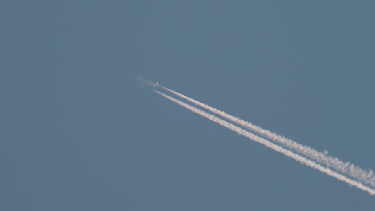 Airplane flying high above leaving long contrails in a clear blue sky