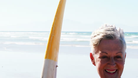 mujer mayor con una tabla de surf de pie en la playa