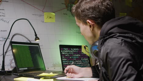 young caucasian man working on laptop, making notes on paper and typing on keyboard