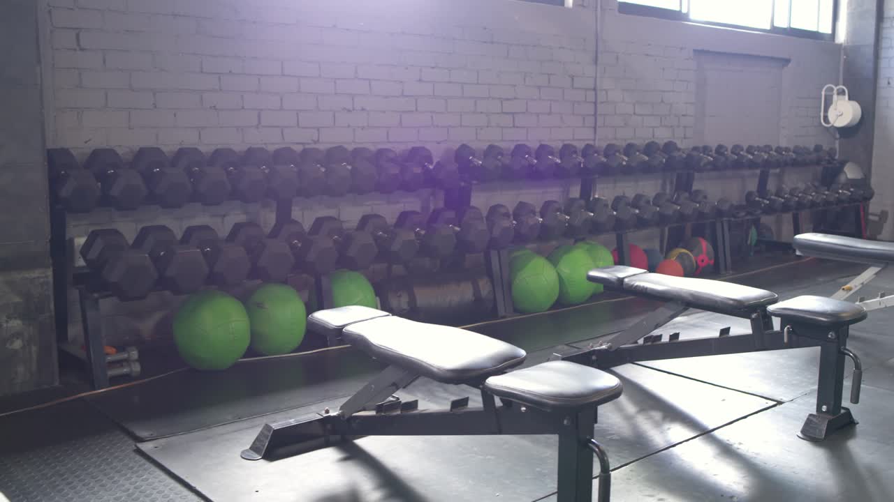 Camera is panning right and down, revealing bench, dumbbells and plyo box, showing studio layout