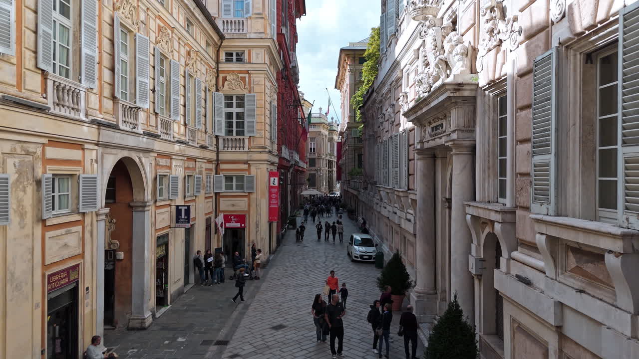 Via Garibaldi in port city Genoa with pedestrians exploring, drone pullback