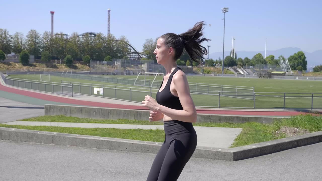 joven mujer caucásica deportiva corriendo alrededor del campo de deportes slomo